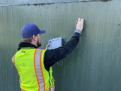 Technician taking an ultrasonic shell thickness reading on a welded-steel water tank