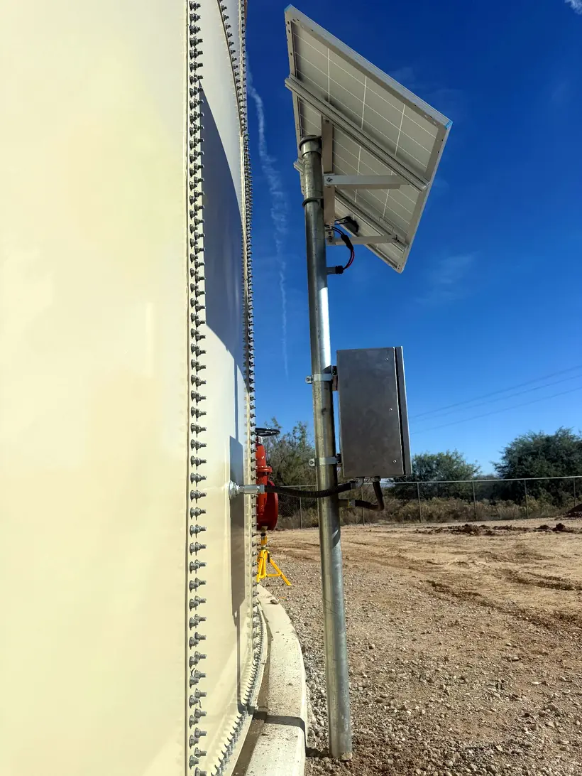 Solar module on a post beside the shell of a bolted steel tank in desert scrub