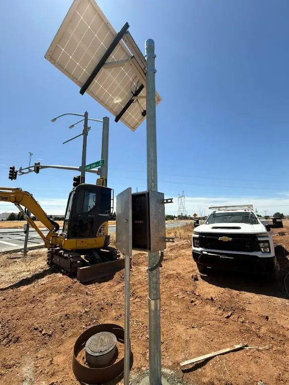Pole-mounted solar module and controller cabinet at a roadway pipeline crossing during construction
